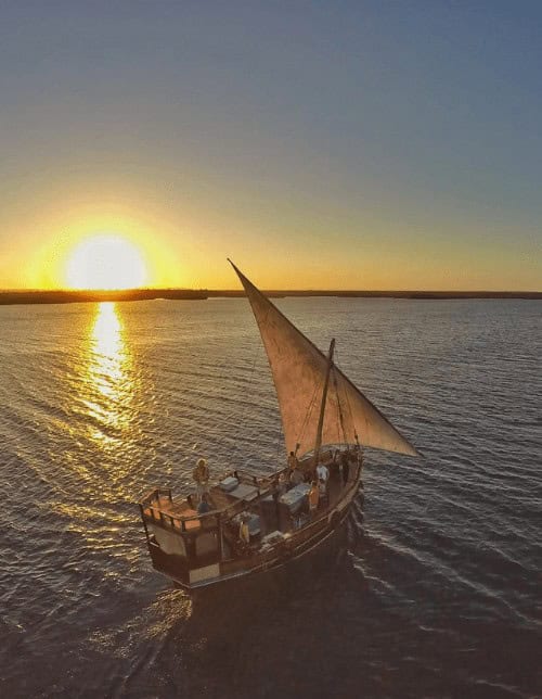 The Holiday Boat, a traditional dhow sailboat, gliding across calm waters at sunset in Watamu, Kenya