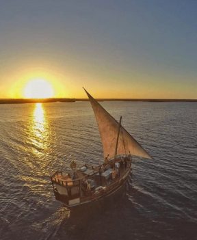 The Holiday Boat, a traditional dhow sailboat, gliding across calm waters at sunset in Watamu, Kenya